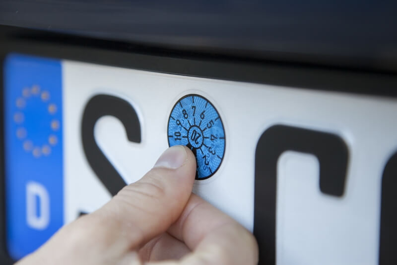 HU (mit integrierter AU) Eine Hauptuntersuchungsplakete, die auf ein Nummerschild geklebt wird